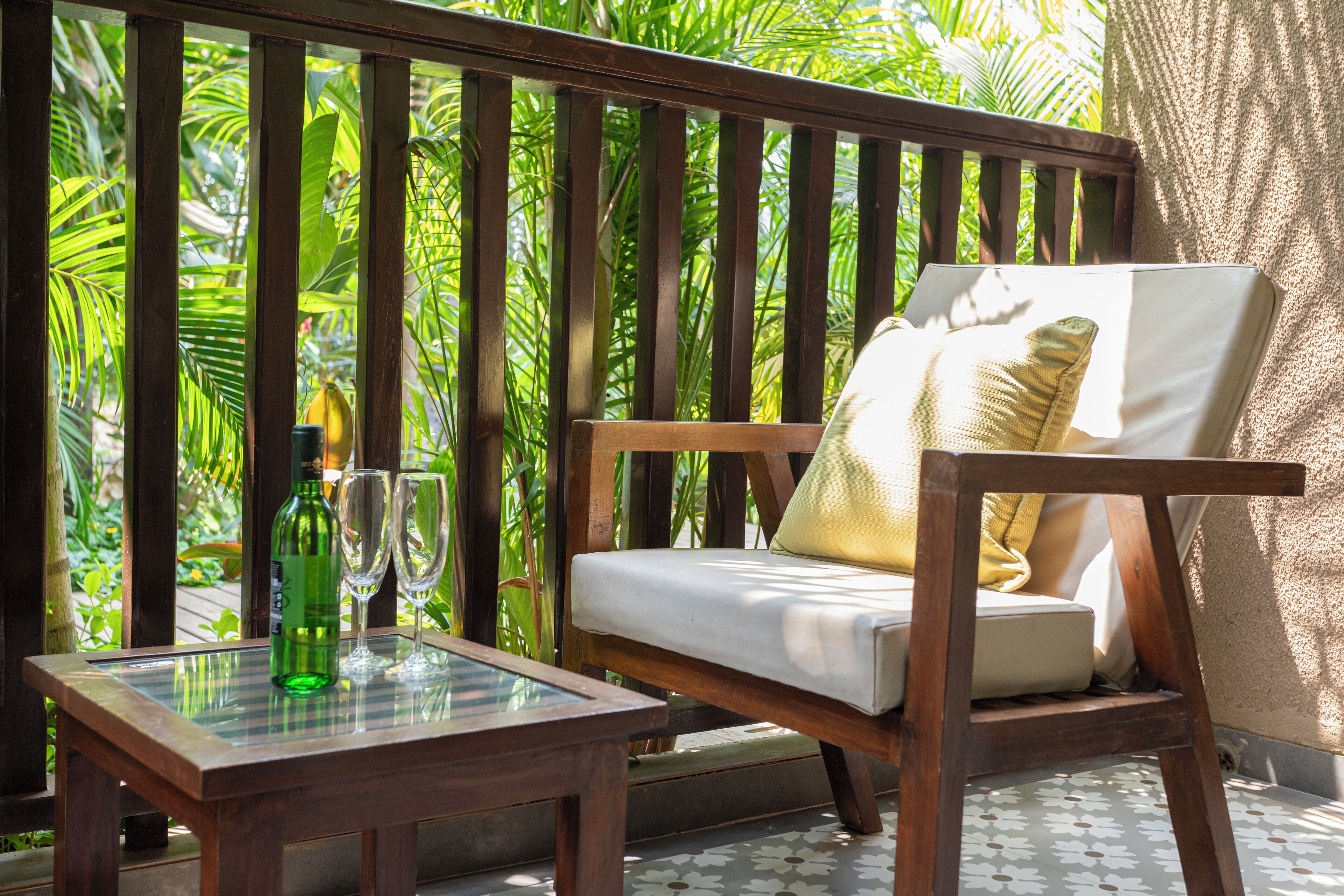 A wooden bench with a cushion and a glass table with a bottle and glasses.
