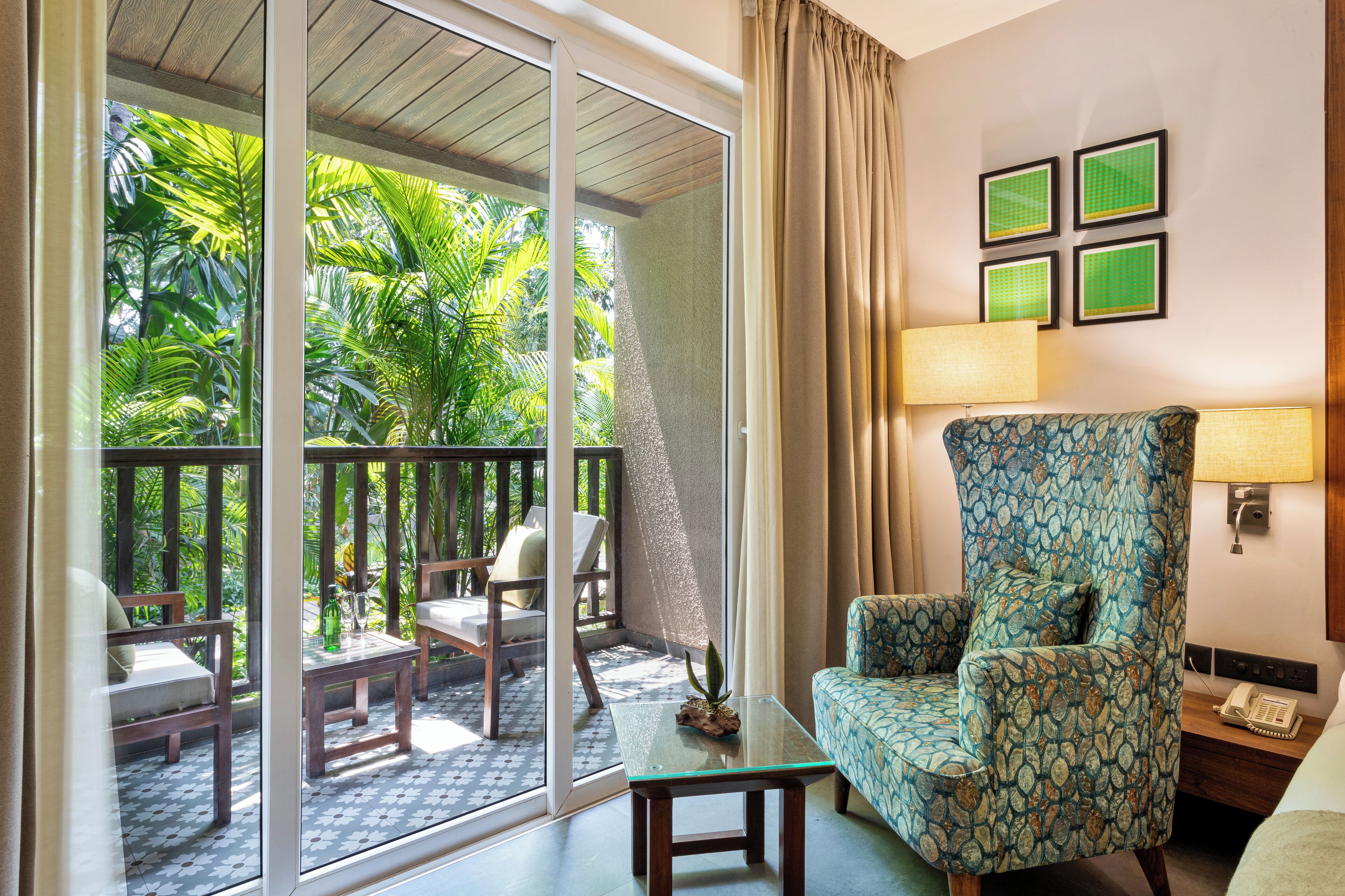 A room with a sliding glass door leading to a balcony with outdoor furniture and lush greenery.