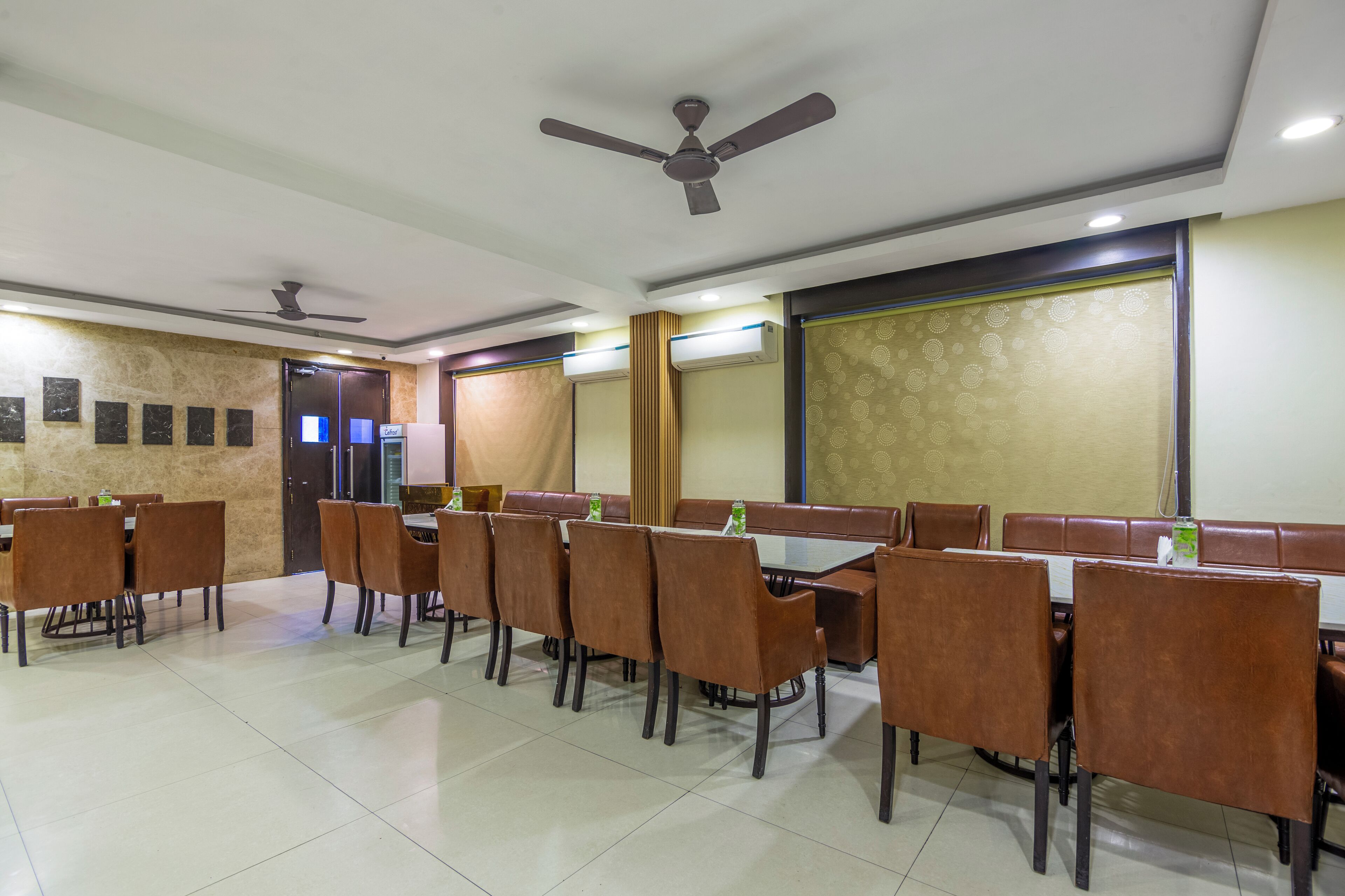 Uma sala de conferências com uma mesa comprida, cadeiras marrons, ventiladores de teto e aparelhos de ar condicionado.