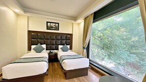 Ein Hotelzimmer mit zwei Betten, Holzboden, einem großen Fenster mit Blick auf Bäume und einem kleinen Tisch.