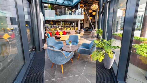 A modern indoor space with a glass ceiling, seating area with chairs, a bar, and a staircase.