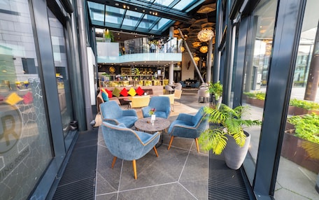 A modern indoor space with a glass ceiling, seating area with chairs, a bar, and a staircase.