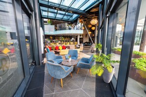 Un espacio interior moderno con techo de vidrio, zona de estar con sillas, un bar y una escalera.