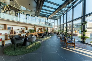 A modern interior with a glass ceiling, wooden shelves with books and plants, and seating areas with tables and chairs. - Clarion Hotel The Edge (Tromsø)