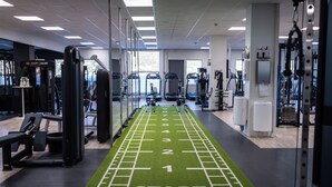 Un gimnasio con pista de correr verde, máquinas de ejercicio y un espejo grande.