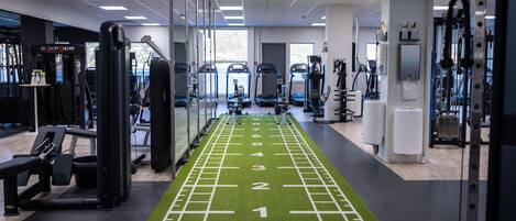 A gym with a green running track, exercise machines, and a mirrored wall.