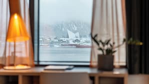 Una habitación con vistas a un paisaje nevado a través de una ventana, una lámpara sobre un escritorio y una planta en maceta.