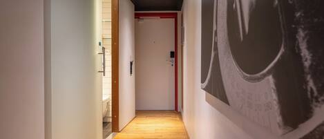 Un pasillo con suelo de madera, una puerta roja al final y una gran obra de arte blanco y negro en la pared derecha.