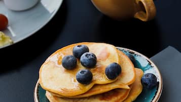 Una pila di pancake con mirtilli su un piatto, una tazza di tè e un croissant su un tavolo.