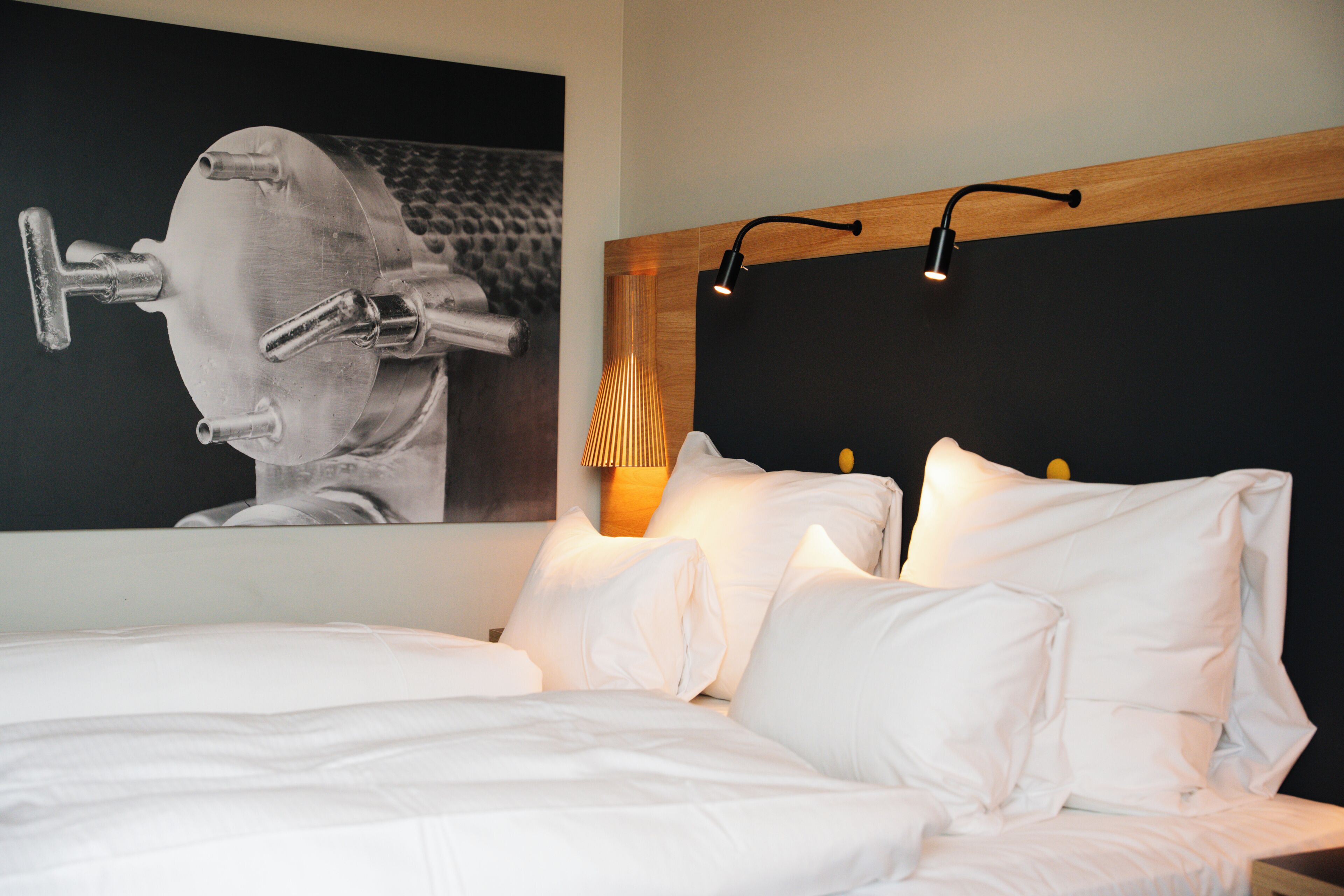 Una cama bien hecha con sábanas blancas, cabecero con iluminación integrada y una obra de arte colgada en la pared.