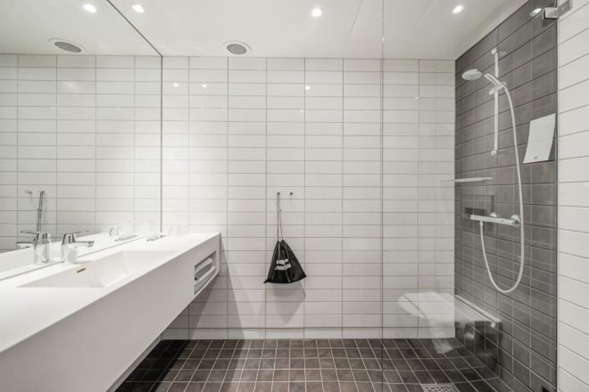 Un baño moderno con un tocador blanco, ducha y una toalla negra colgada en un perchero.