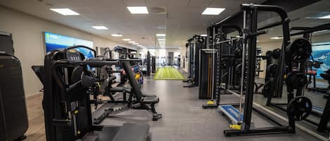 A gym with various exercise equipment, a mirrored wall, and a green running track in the center.