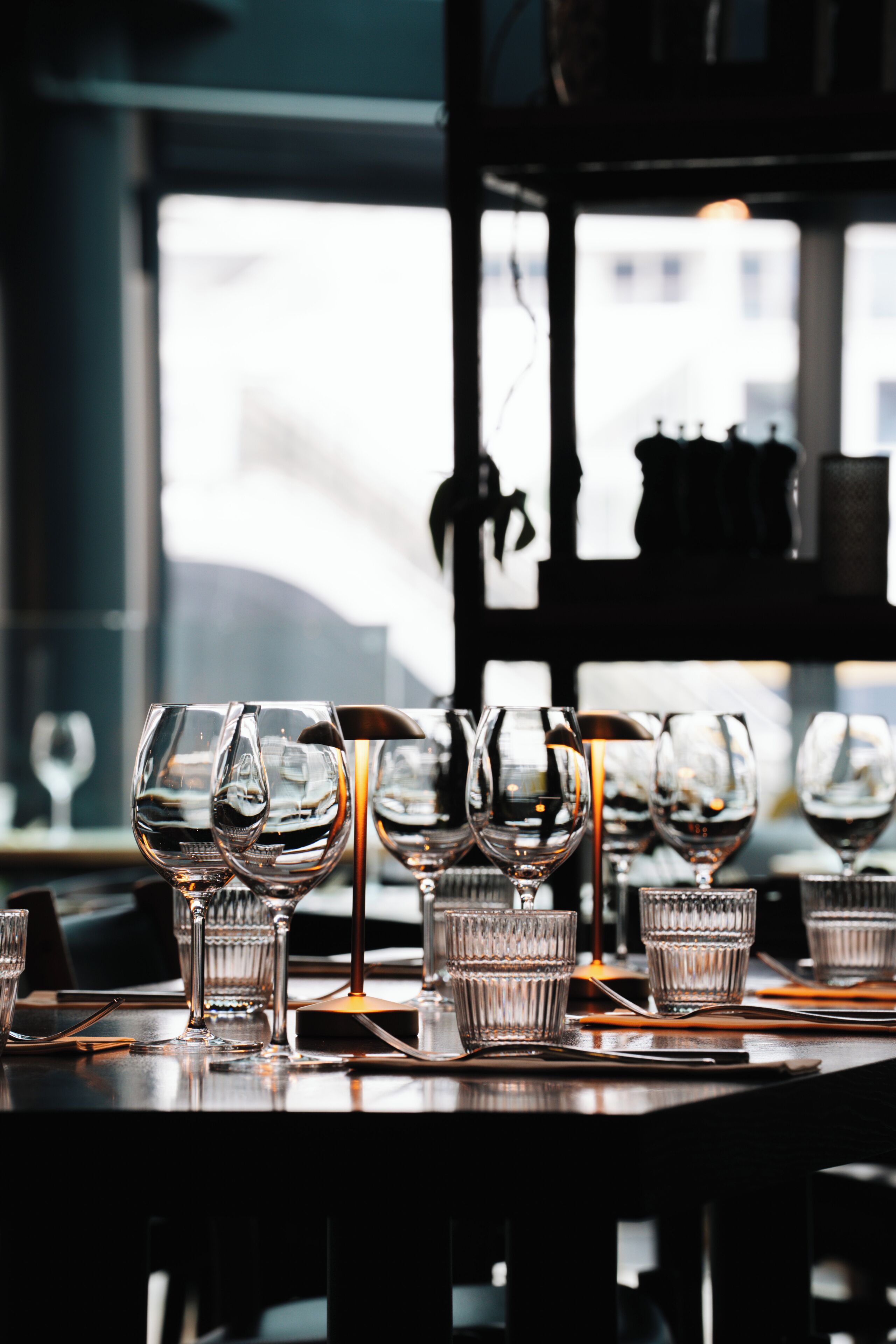 A bar setting with multiple glasses and a bottle, a window with a view, and a shelf with items.