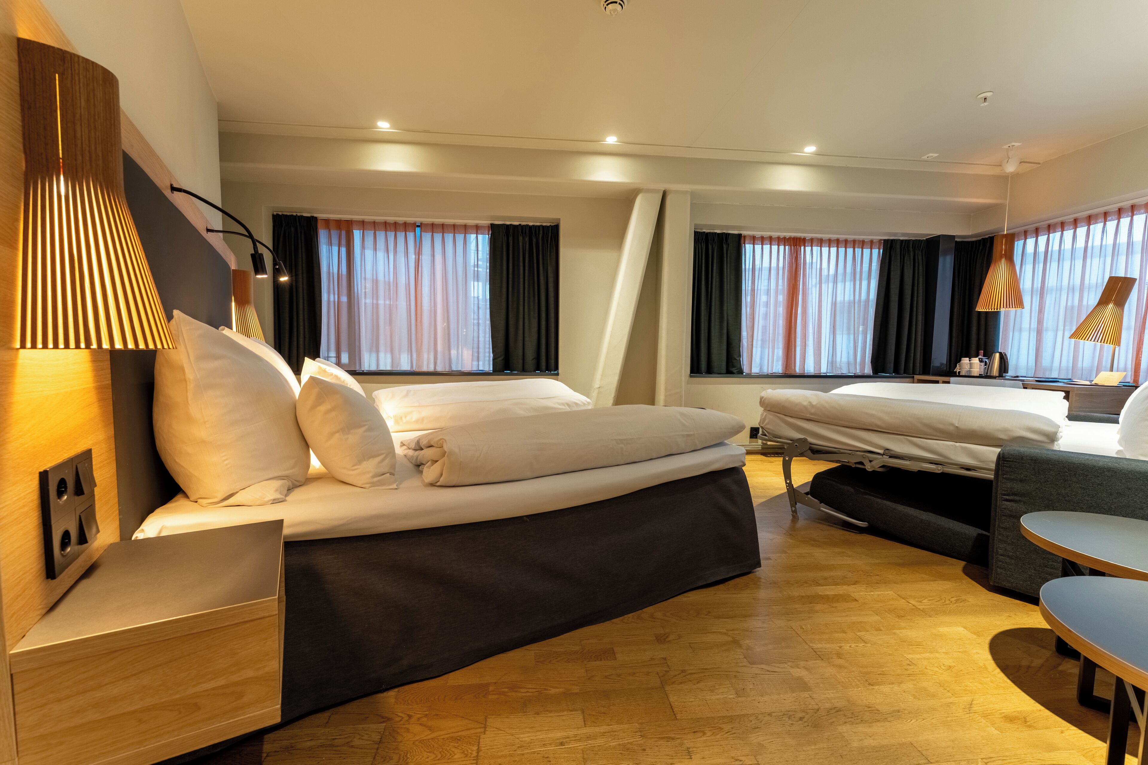 A hotel room with two beds, a desk, a chair, and a table.