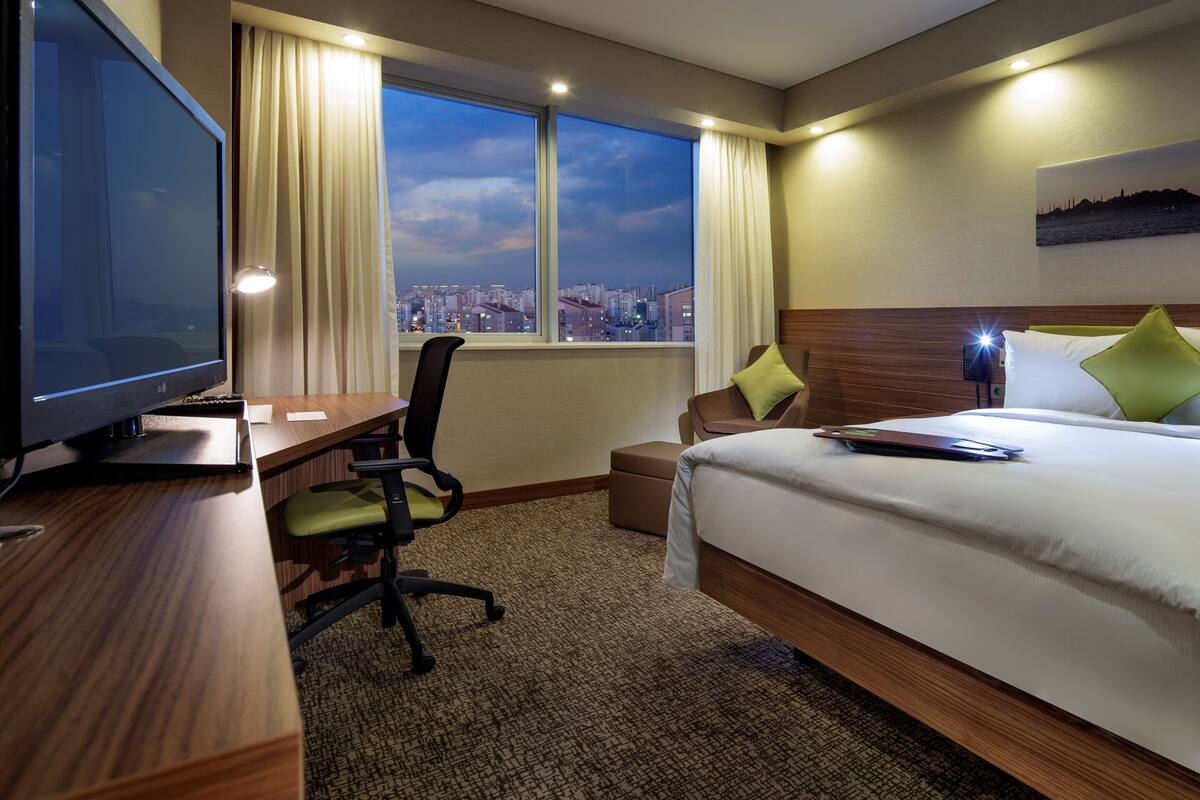 Habitació d'hotel amb un llit, un escriptori amb televisió, una cadira, una finestra que donava a una vista de la ciutat i un quadre penjat a la paret.