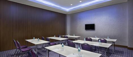 Un salón de conferencias con mesas, sillas y un televisor de pantalla plana en la pared.