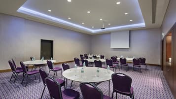A conference room with round tables, purple chairs, and a projector screen.