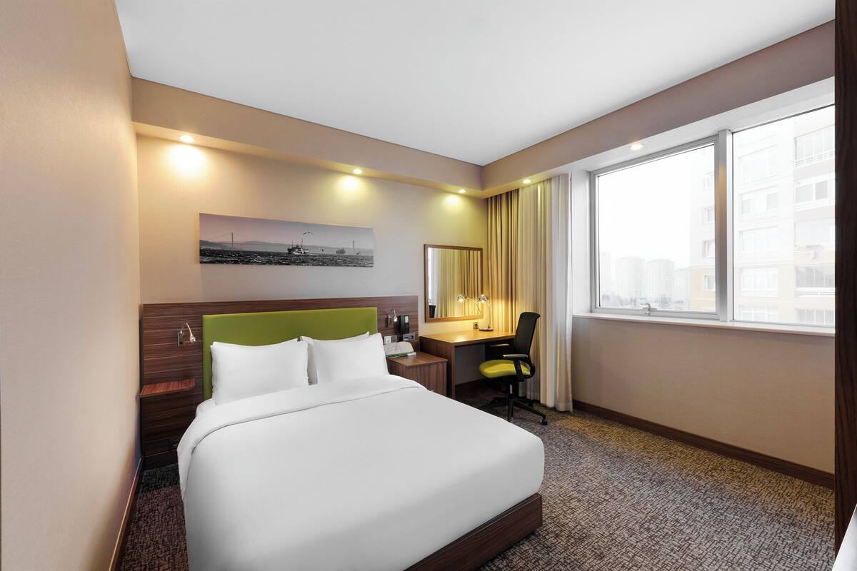 Habitació d'hotel amb llit, escriptori, cadira i una finestra gran.