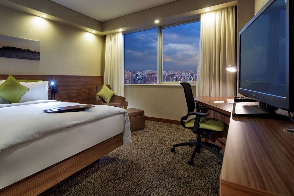 Habitació d'hotel amb un llit, escriptori, cadira, televisió i finestra amb vista a la ciutat.