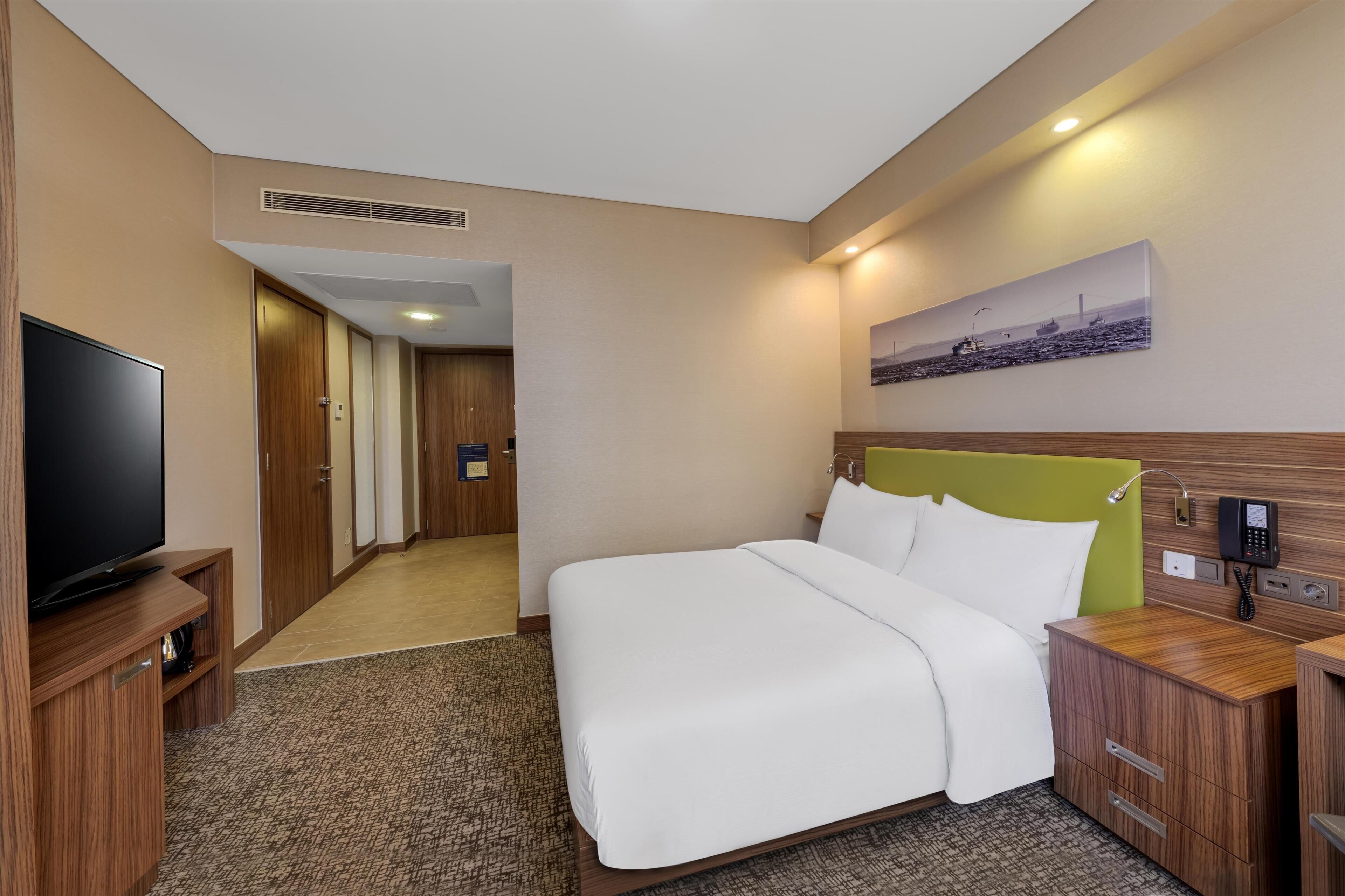 Een hotelkamer met een bed, een televisie, een schilderij aan de muur en een gang naar een andere kamer.