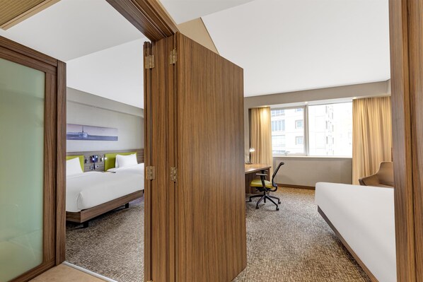 A hotel room with a bed, a desk, a chair, and a view of buildings through the window.