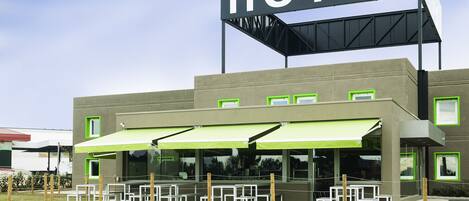A modern hotel with a prominent 'HOTEL' sign, outdoor seating area, and a covered patio.