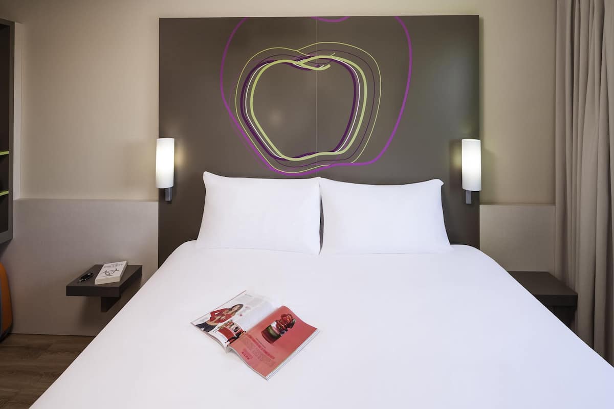A hotel room with a large bed, two bedside tables, a magazine on the bed, and a decorative wall art piece.