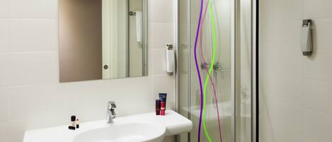 A modern bathroom with a white sink, mirror, and glass shower enclosure.