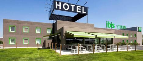 A modern hotel with a prominent 'HOTEL' sign, outdoor seating area, and 'ibis Styles' branding.