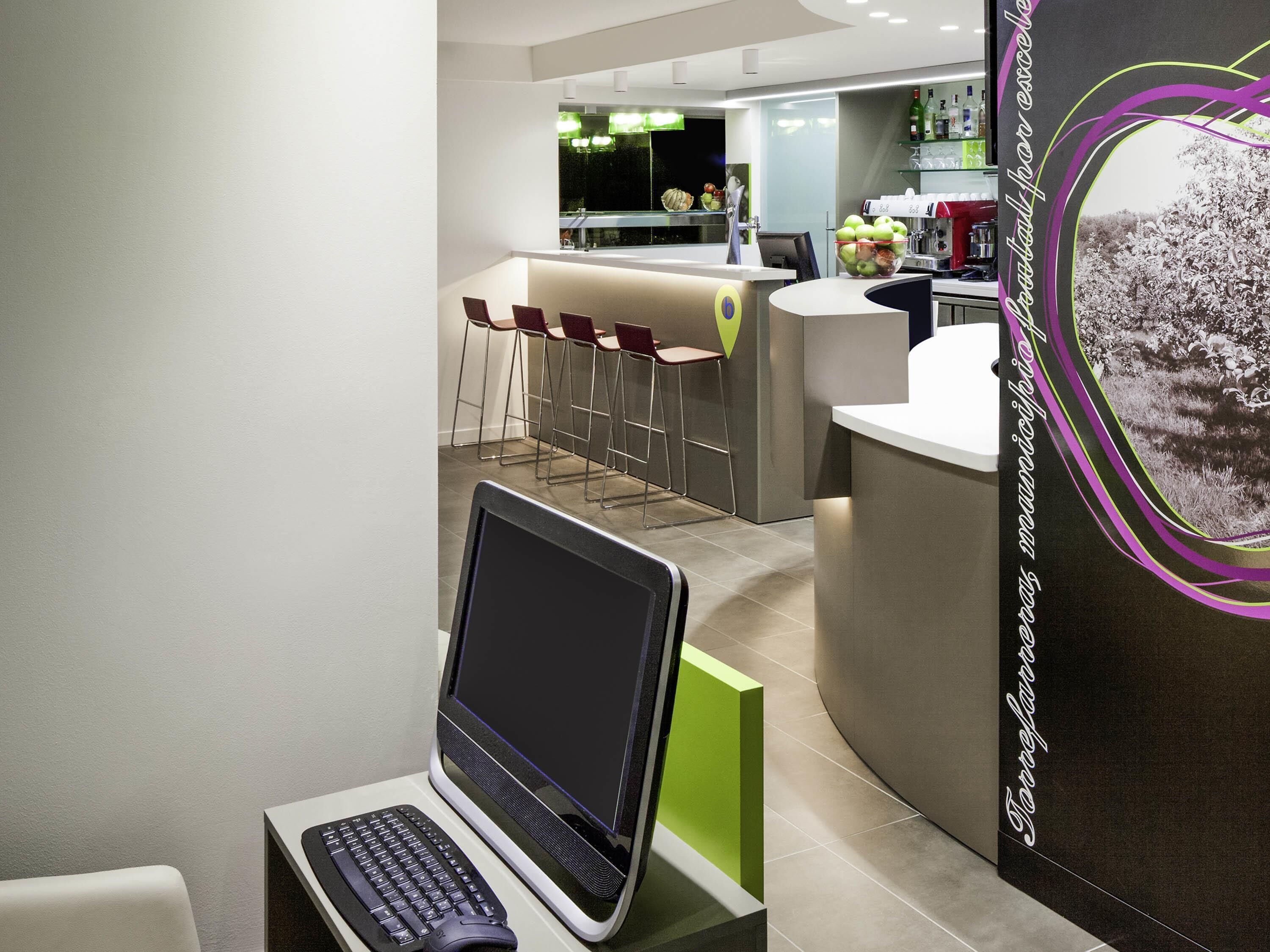 Una moderna hall d'albergo con area bar, posti a sedere e un laptop su un supporto.