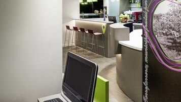Una moderna hall d'albergo con area bar, posti a sedere e un laptop su un supporto.