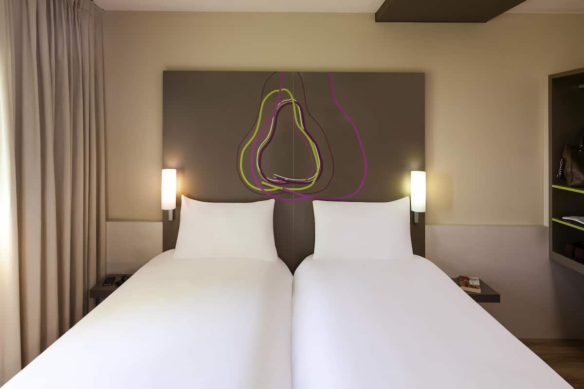 Ein Doppelbett mit weißer Bettwäsche, zwei Nachttische, eine Wandleuchte und ein dekoratives abstraktes Kunstwerk darüber.