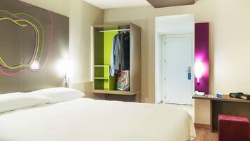 Ein Hotelzimmer mit Bett, Schrank, Schreibtisch mit Stuhl und einer Tür.