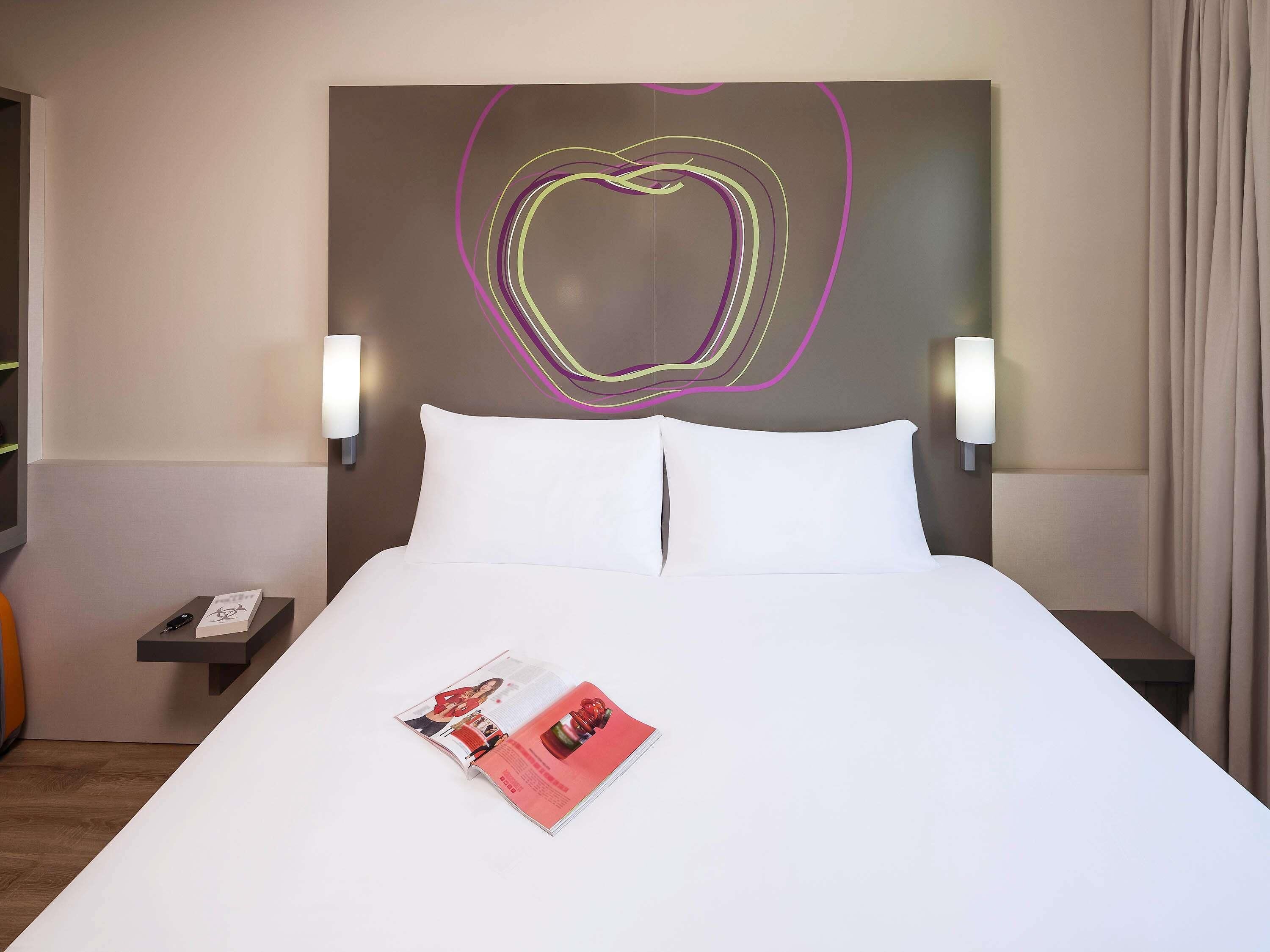 Ein Hotelzimmer mit einem großen Bett, zwei Nachttischen, einem Wandbild und einer Zeitschrift auf dem Bett.