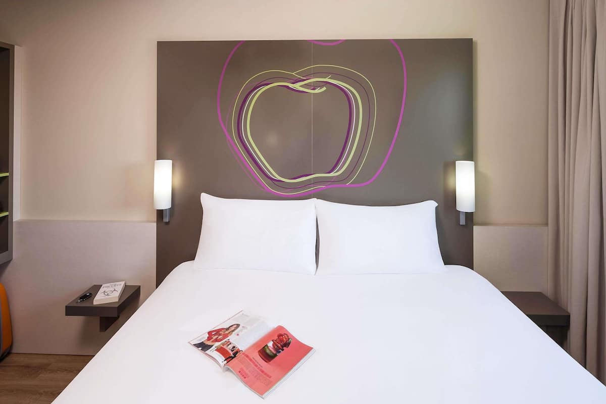 Ein Hotelzimmer mit einem großen Bett, zwei Nachttischen, einem Wandbild und einer Zeitschrift auf dem Bett.