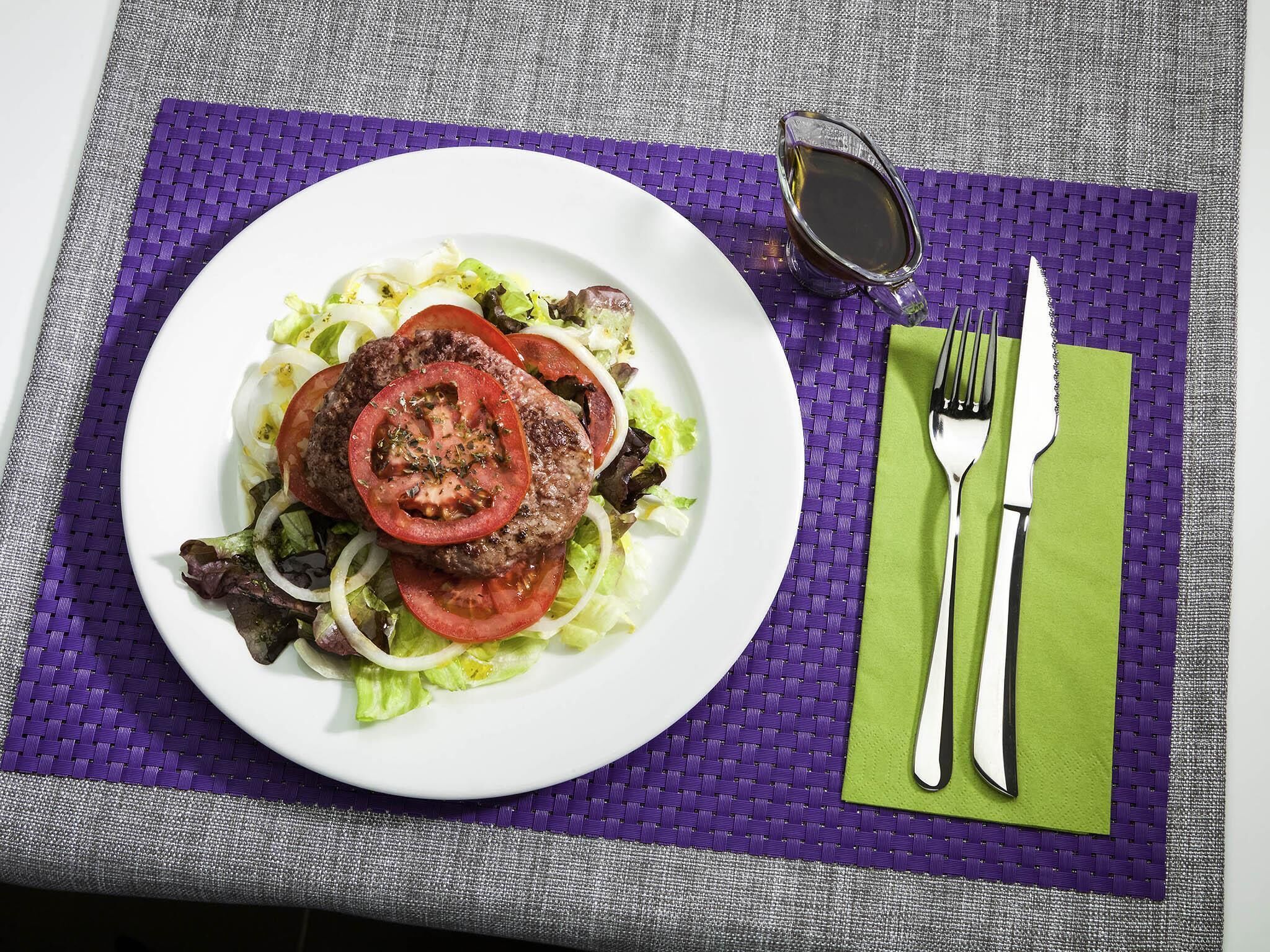Plat de menjar amb una hamburguesa i amanida sobre un plat blanc, posat sobre un suport de tela morat.