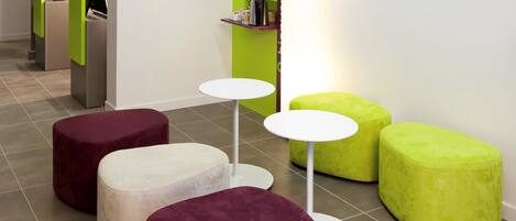 Un interior moderno con asientos acolchados redondos en tonos morado y verde, mesas blancas y una pared de acento verde brillante.