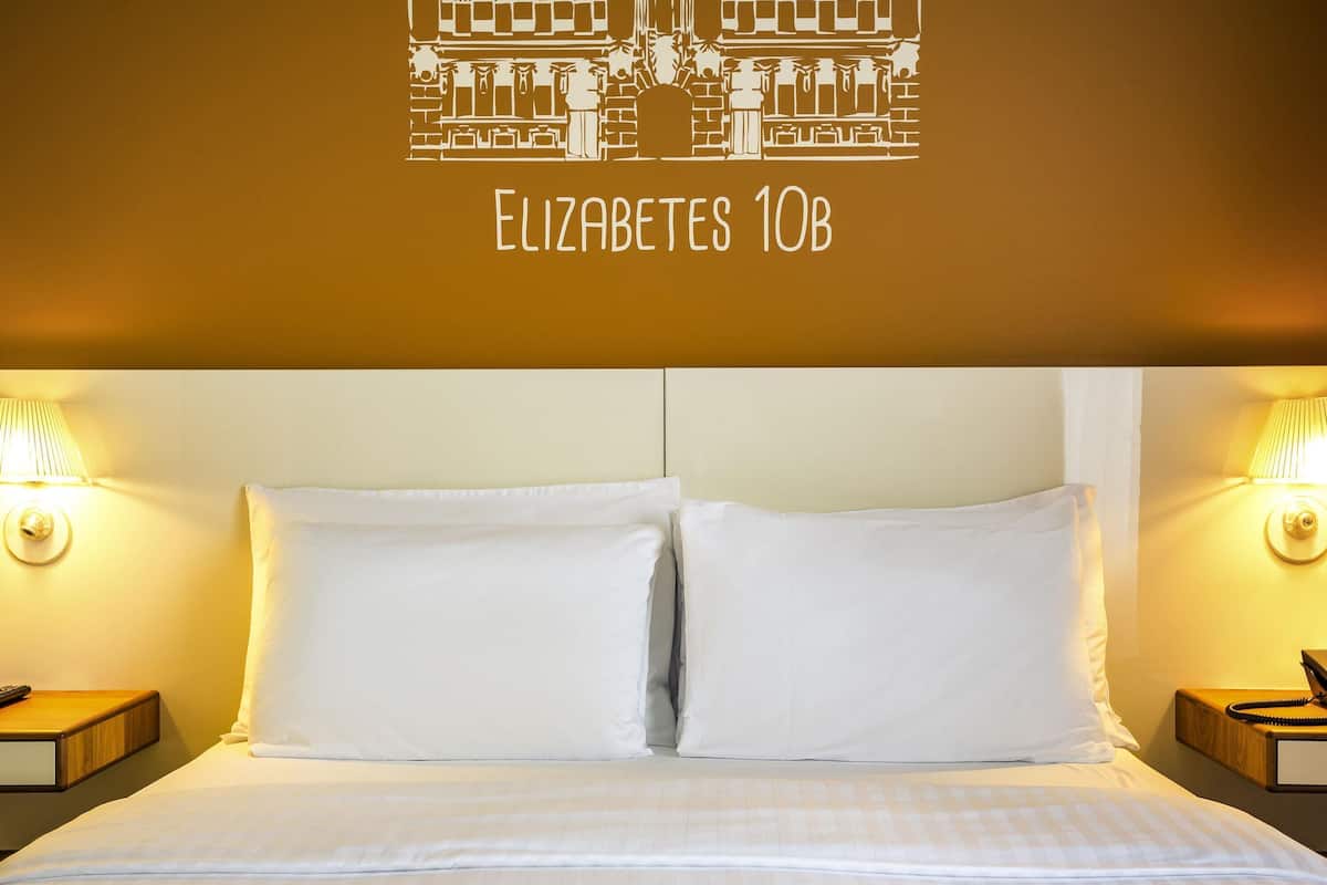 Une chambre d’hôtel avec un grand lit, deux tables de chevet et une lampe fixée au mur.