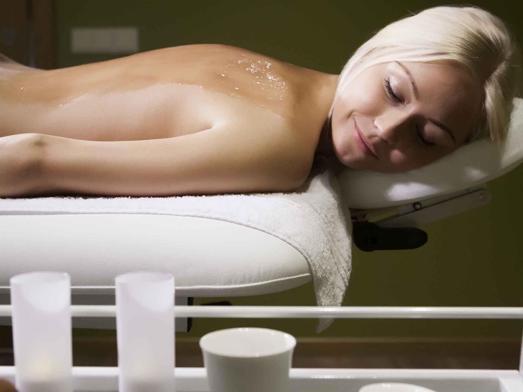 A person lying on a massage table in a room with a white chair and a white wall.