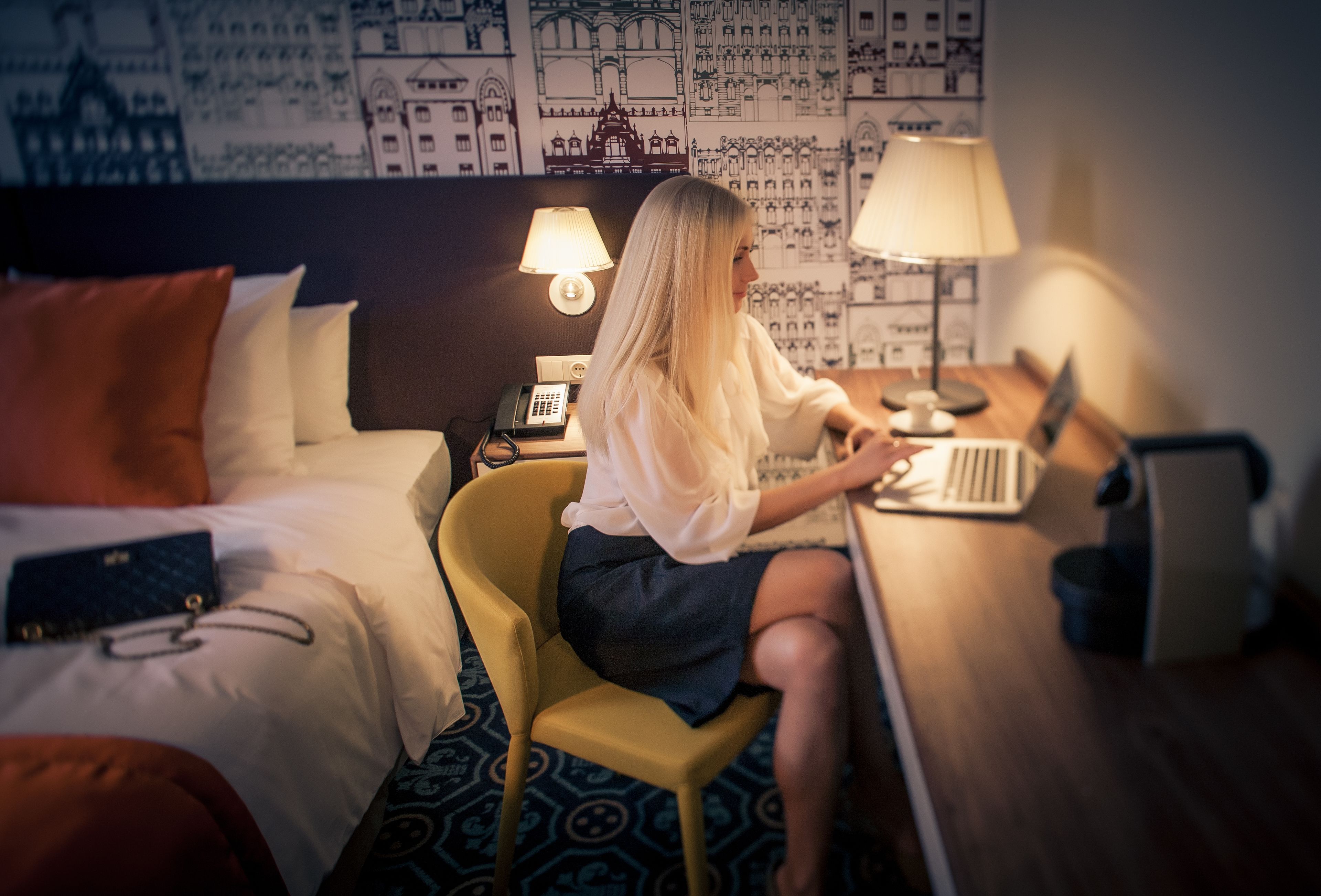 Una habitación de hotel con una cama, un escritorio con una computadora portátil, una lámpara y un teléfono.