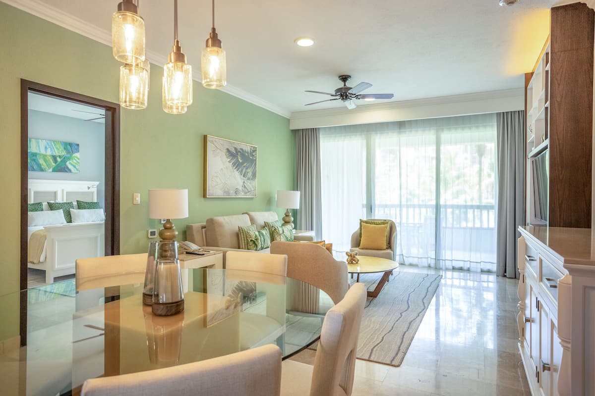 A spacious living room with a glass dining table, comfortable seating, a ceiling fan, and large windows with curtains.