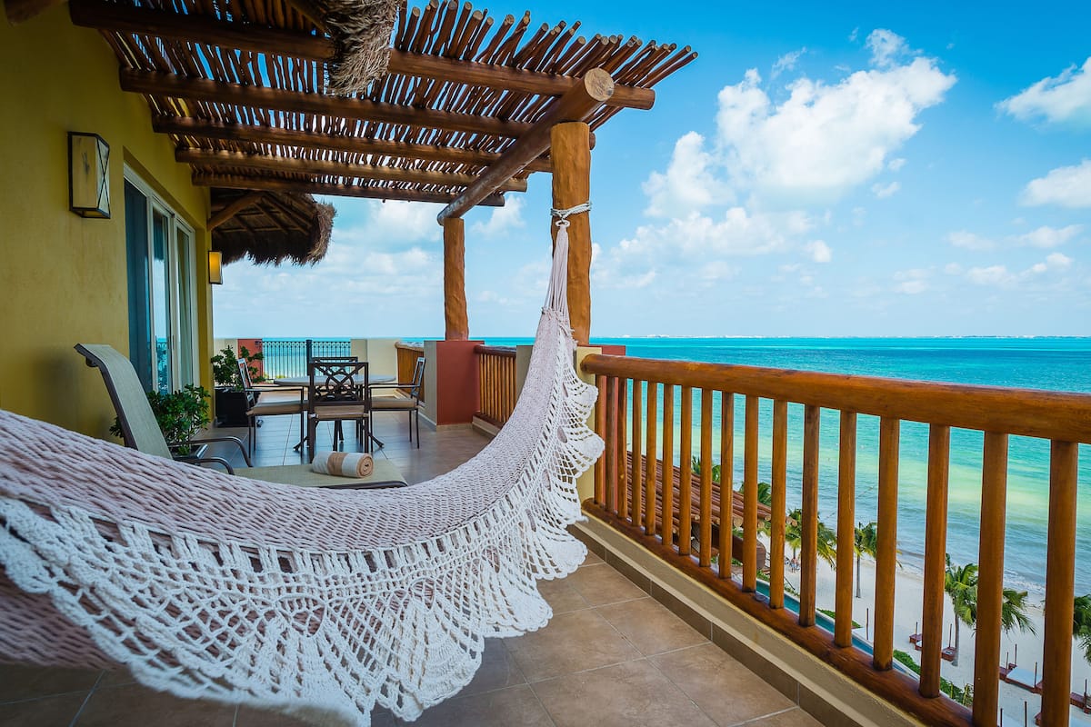 A balcony with a hammock, wooden railing, and a view of the ocean.