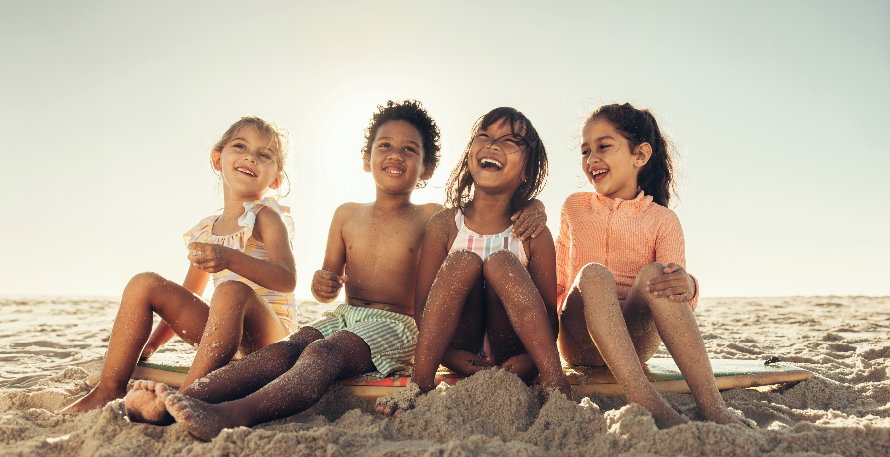 Quatre enfants assis sur une planche de surf, sur une plage de sable.