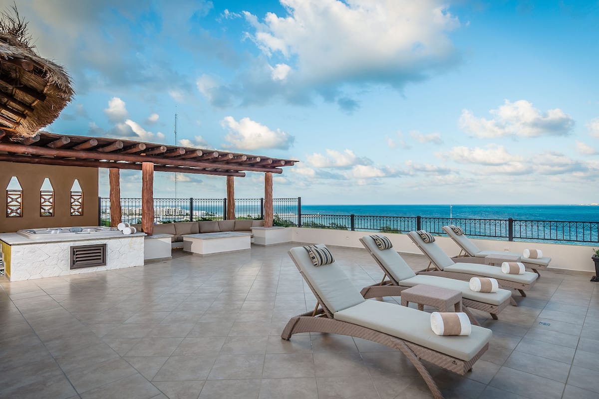 A sunlit outdoor lounge area with a pool, lounge chairs, and a view of the ocean.