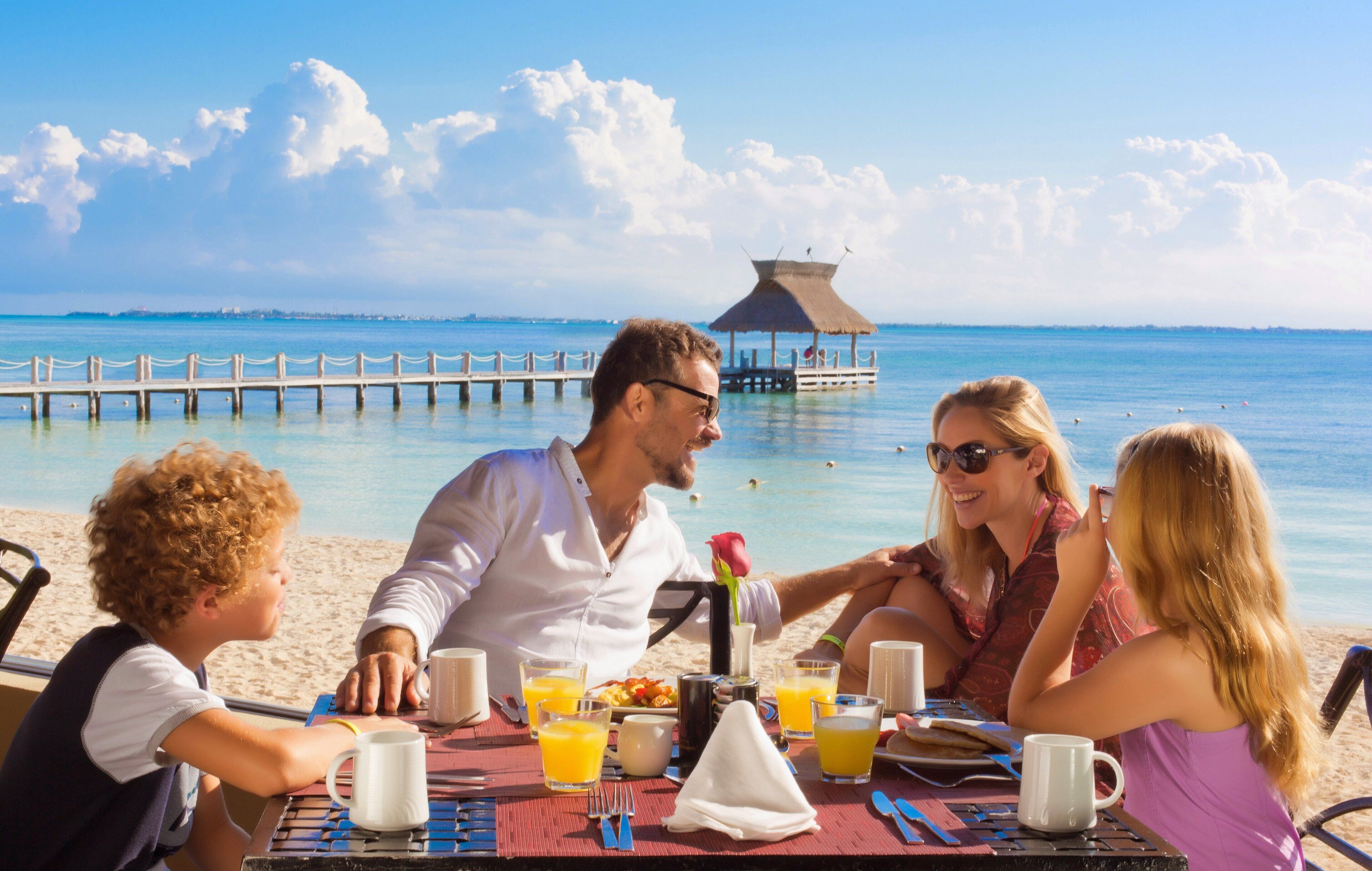 A family dining at a table with a view of the ocean and a pier in the background.