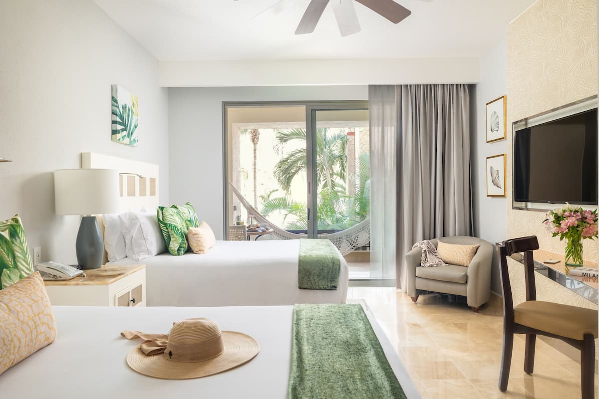 A hotel room with a bed, a desk, a chair, a TV, and a view of palm trees.