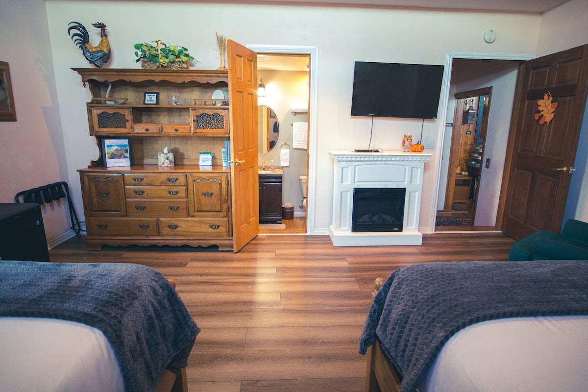 A bedroom with two beds, a wooden dresser, a television, and a fireplace.