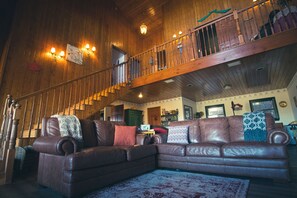 A spacious living room with a large brown leather sectional sofa, a wooden staircase, and a chandelier. - Tucker Peak Lodge (Julian)