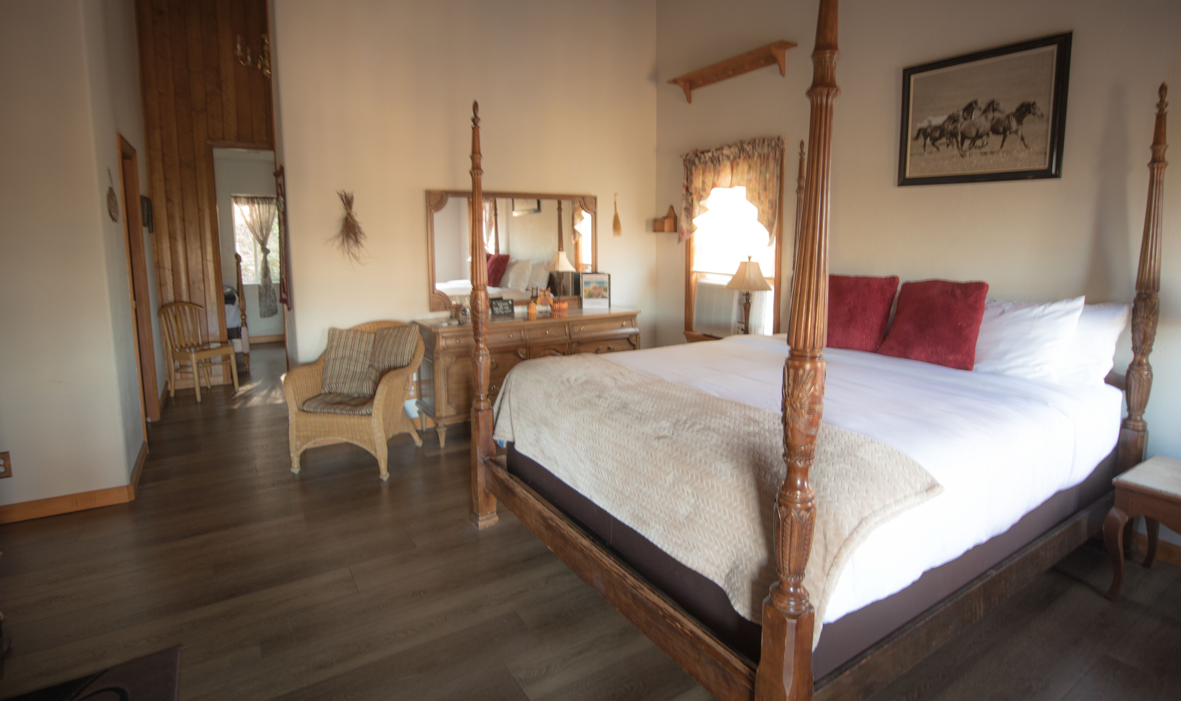 Une chambre spacieuse avec un grand lit, une tête de lit en bois sculptée, une commode en bois, une chaise et un miroir.