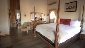 Une chambre spacieuse avec un grand lit, une tête de lit en bois sculptée, une commode en bois, une chaise et un miroir.
